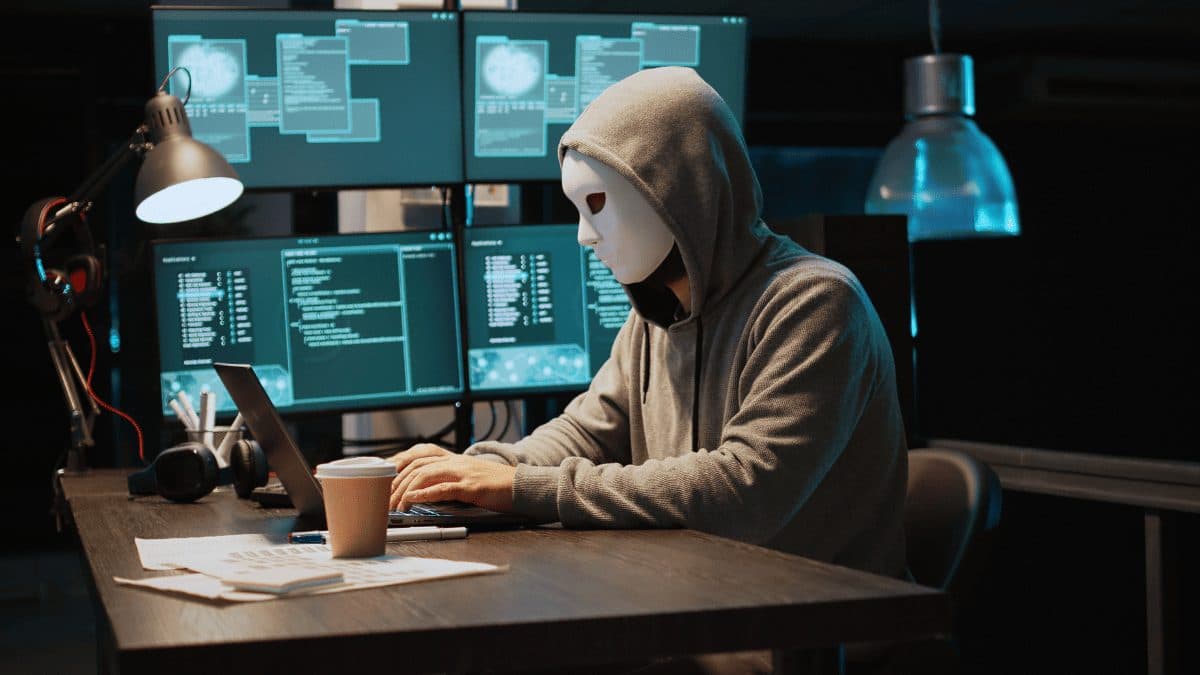 Personne masquée devant des écrans, illustrant la fraude numérique